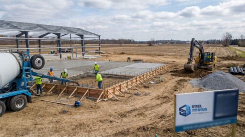 Construction workers preparing a concrete foundation for a metal building.