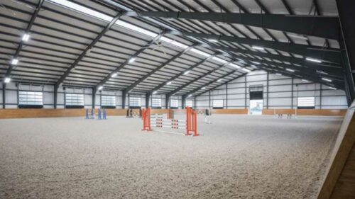 realistic image of an indoor horse riding arena. The arena is empty and has a sand floor.
