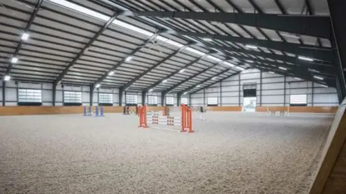 realistic image of an indoor horse riding arena. The arena is empty and has a sand floor.