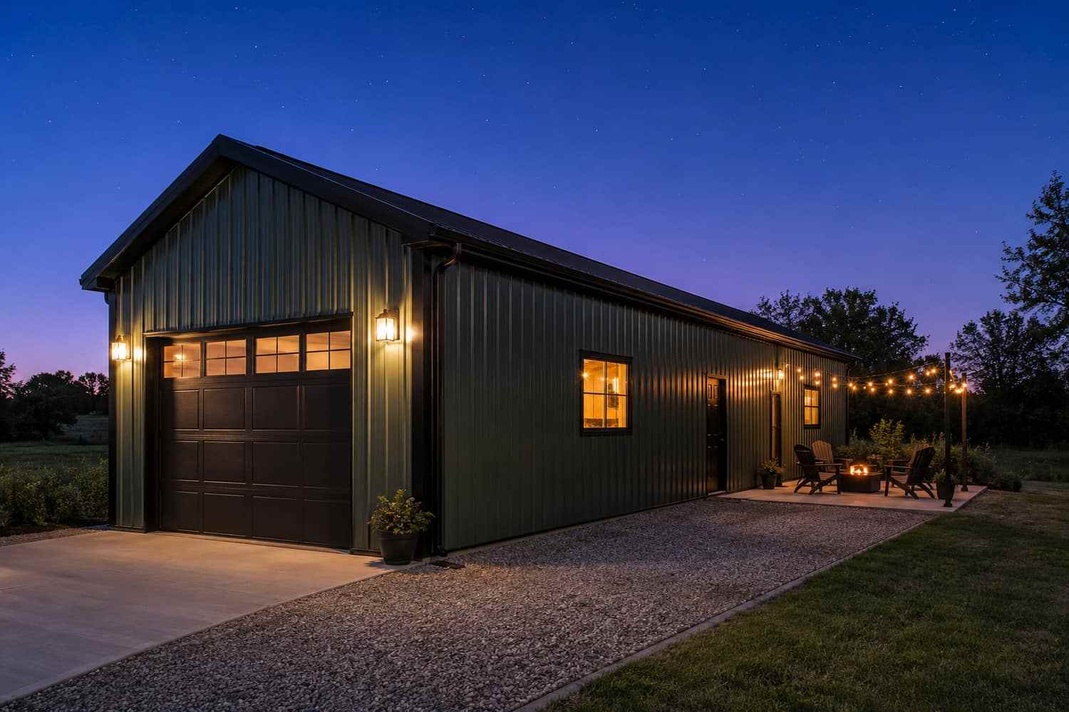 Olive green steel building garage at night with carriage door, string lights, and fire pit