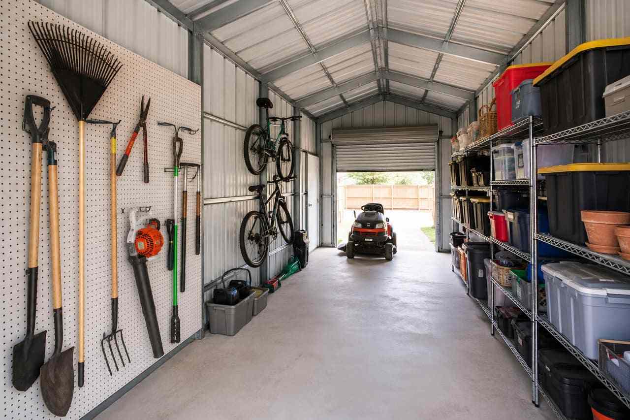 Red steel building storage shed with open roll-up door showing zero turn mower and shelving