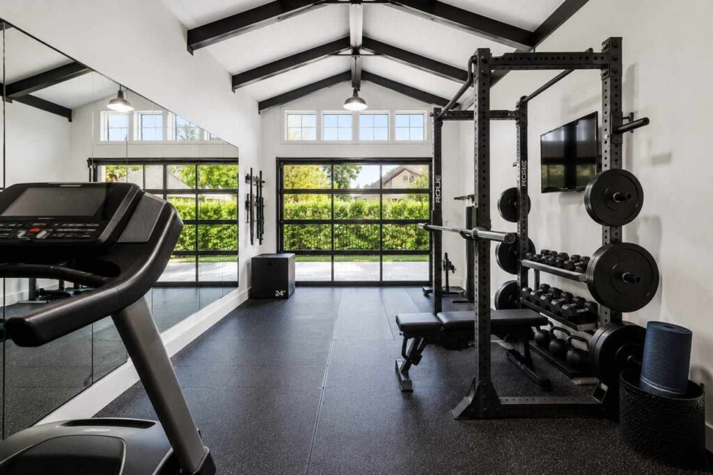 Minimalist home gym interior inside a steel building with power rack, treadmill, and glass door