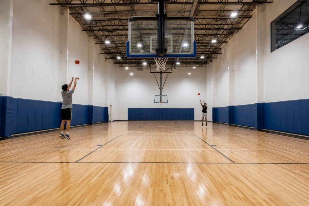 Steel building interior basketball court with wood floor, wall pads, and players shooting