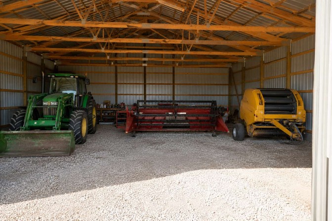 Blue steel carport sheltering pickup trucks and an orange tractor on a farm at sunset