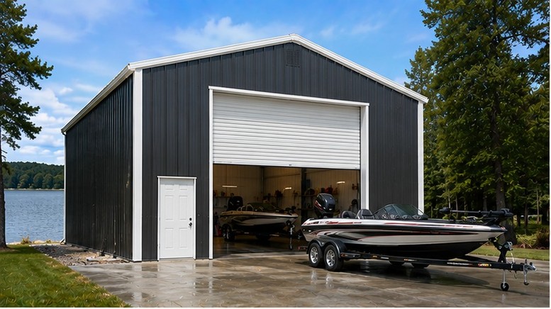 Charcoal steel garage with open roll-up door storing bass boats beside a quiet lake