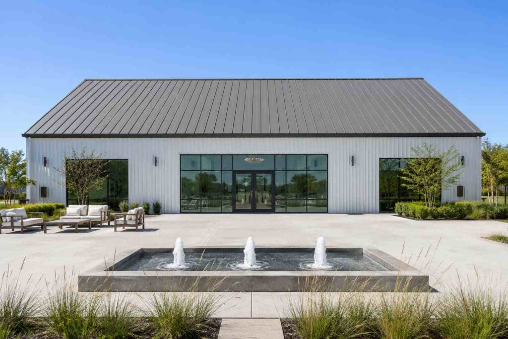 White steel structure event venue with black-framed glass entry and fountains in a modern courtyard